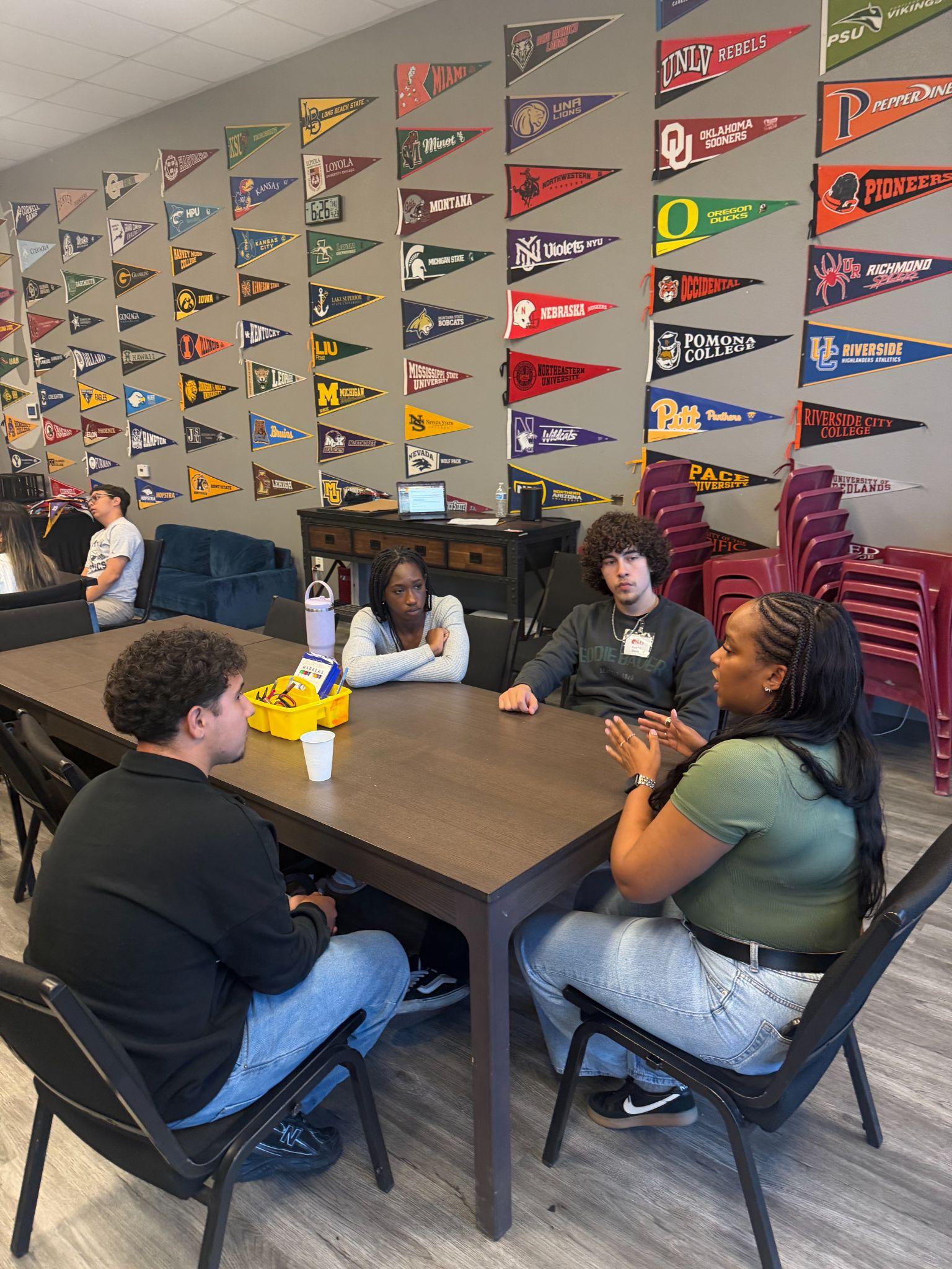 LIT students in a small group discussion beneath a wall of college pennants